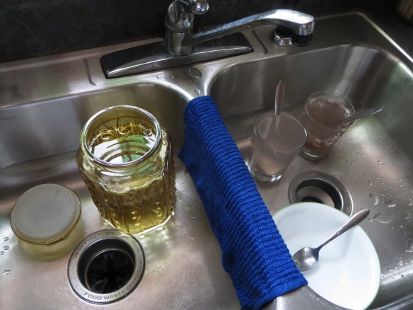glass canister, bowl, and glasses soaking in stainless steel sink